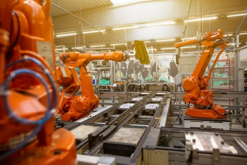 Orange industrial robots operating on an assembly line inside a large manufacturing hall