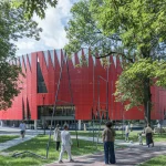 Street-level view of Jihlava Municipal Arena with its zigzagging red aluminium facade among trees