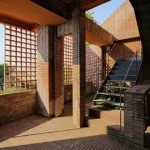 Exterior corner of Common Days with terracotta brick screens and open upper terrace overlooking the landscape