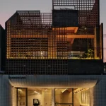 Front elevation of the three-story building showing ground-floor openness and upper-level terracotta screens