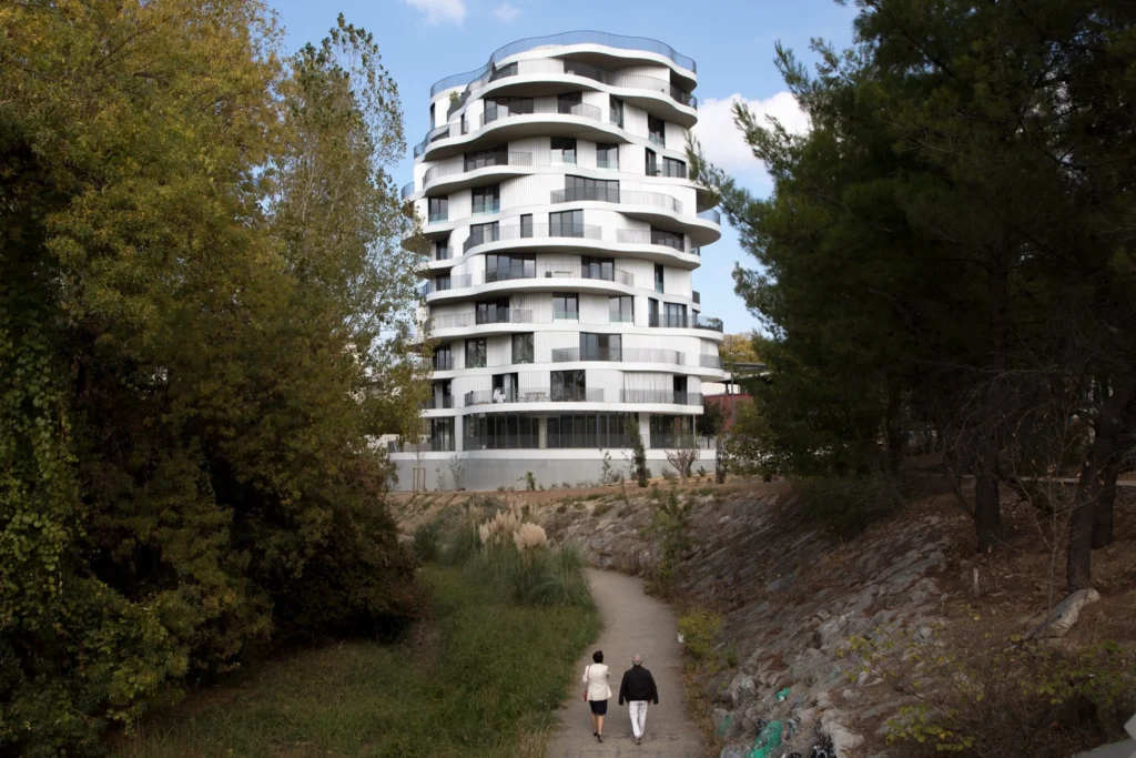White multi-storey residential building with undulating balconies set among trees