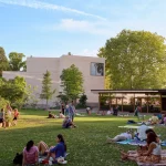 Visitors relaxing on the lawn of the expanded park with new buildings in the background