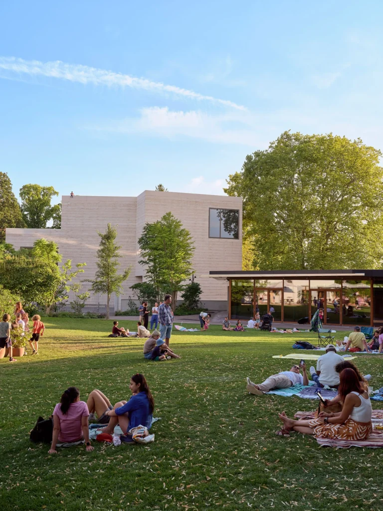 Visitors relaxing on the lawn of the expanded park with new buildings in the background