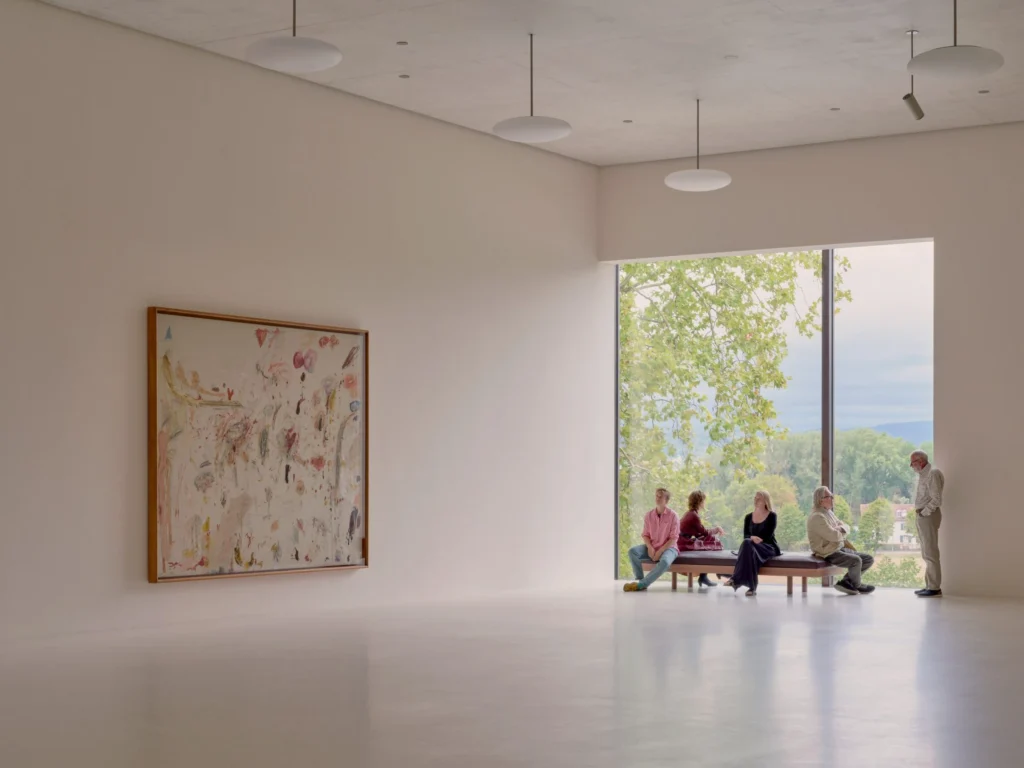 Bright gallery interior with white walls, artwork and a large window overlooking trees