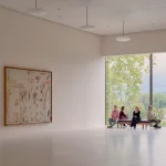 Bright gallery interior with white walls, artwork and a large window overlooking trees