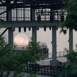 The illuminated sphere seen through the industrial structure of the shipyard pier