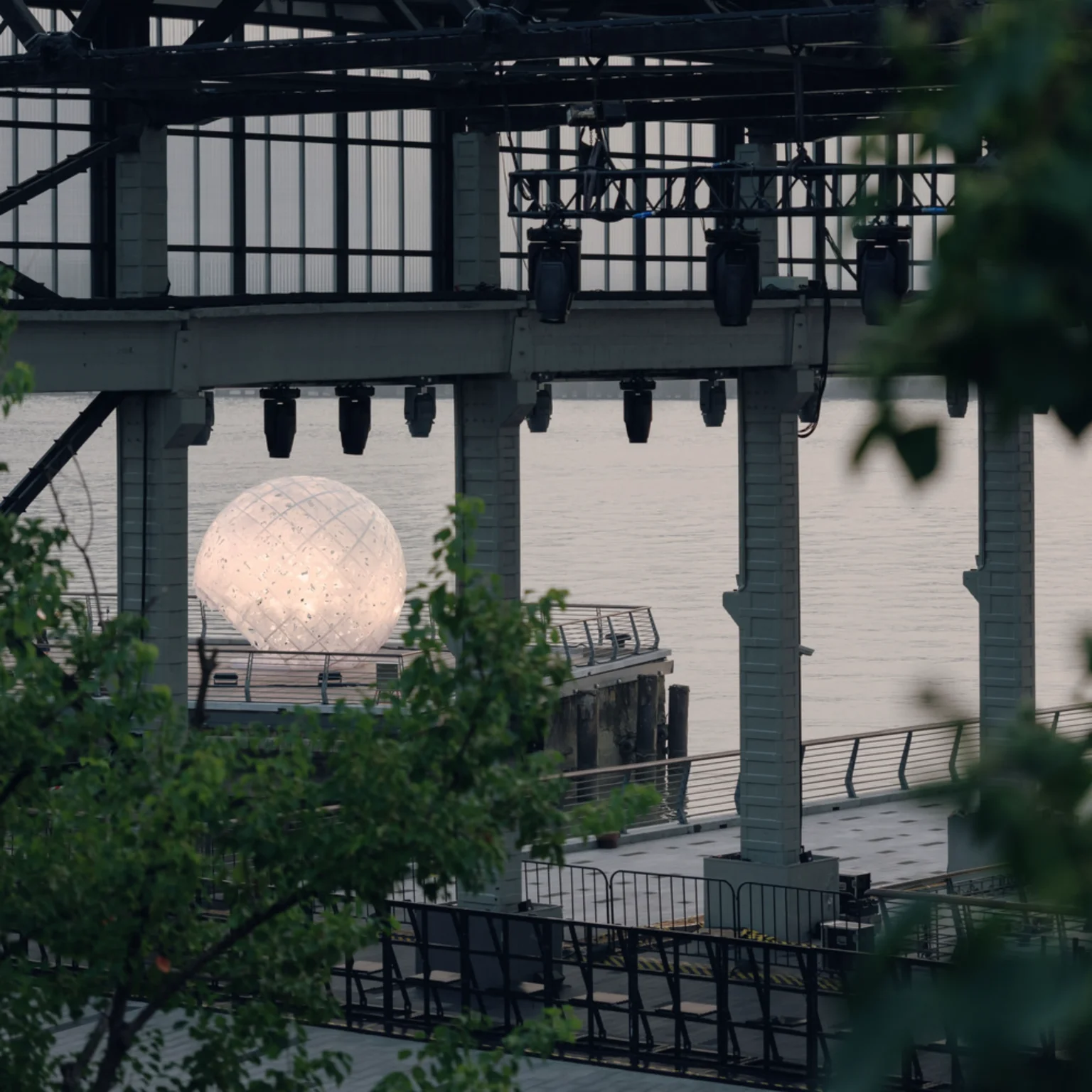 The illuminated sphere seen through the industrial structure of the shipyard pier