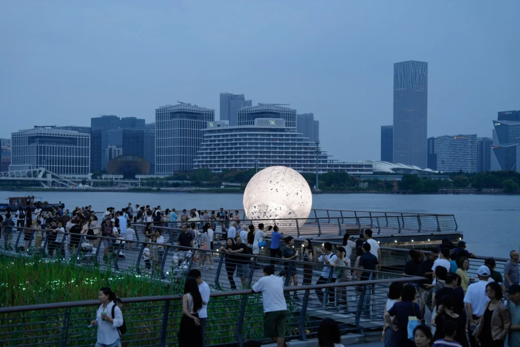 The Full Moon: Crowds on the pier at twilight with the glowing sphere and the Shanghai skyline beyond