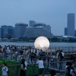 Crowds on the pier at twilight with the glowing sphere and the Shanghai skyline beyond