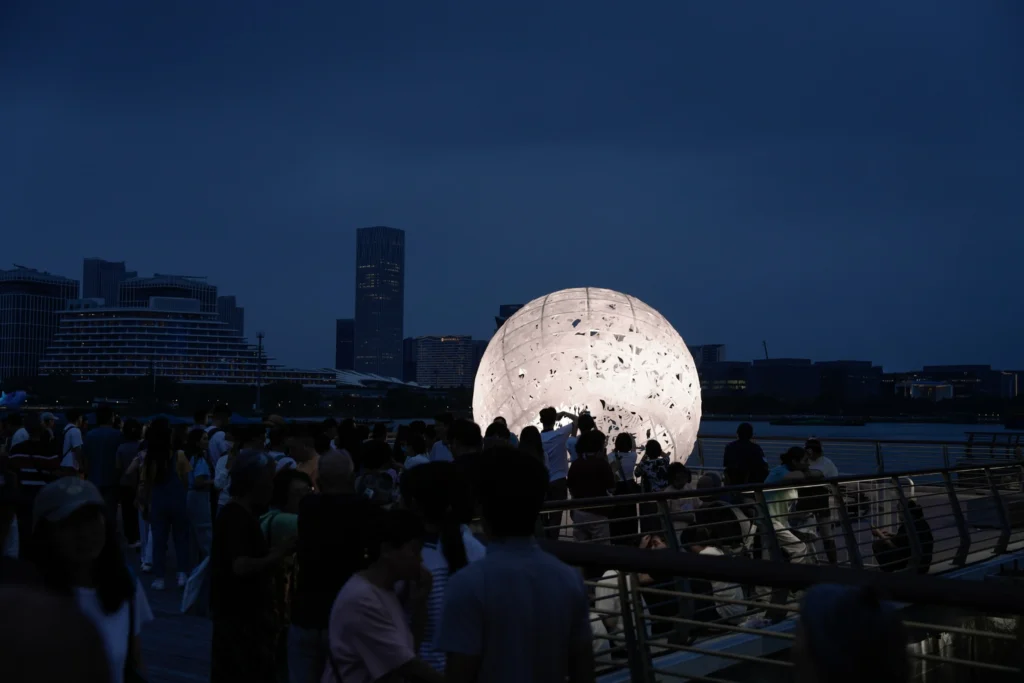 The Full Moon: Night view of the brightly lit sphere surrounded by people on the pier