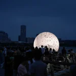 Night view of the brightly lit sphere surrounded by people on the pier