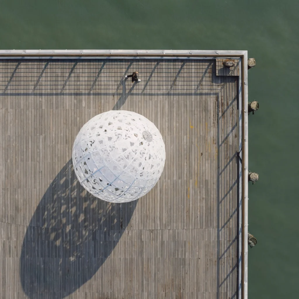 The Full Moon: Aerial view of the white spherical structure casting patterned shadows on the wooden pier
