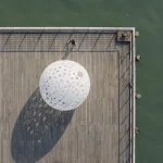 Aerial view of the white spherical structure casting patterned shadows on the wooden pier