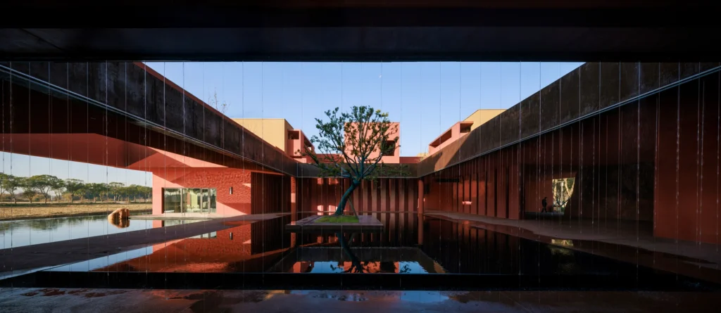 Terracotta walls and volumes casting sharp shadows along a planted pathway