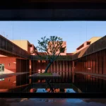 Terracotta walls and volumes casting sharp shadows along a planted pathway