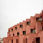 Close-up of the coral-red stucco facade with deep openings and a person standing in a balcony niche