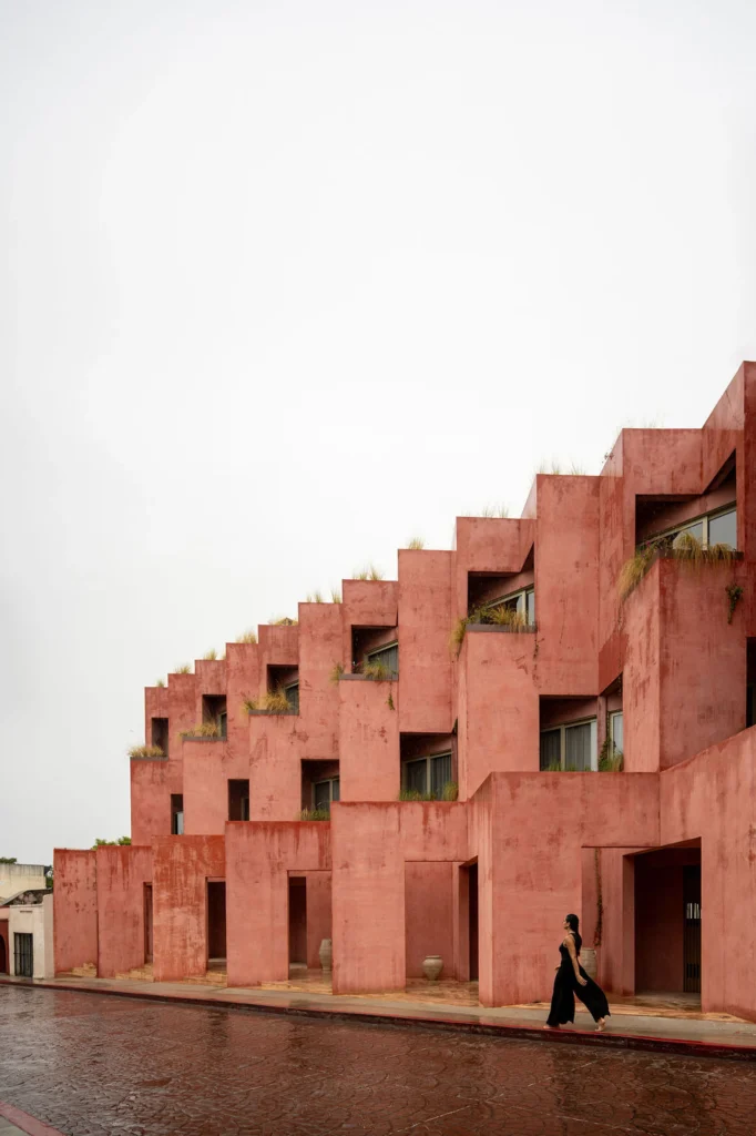 Laiva Plaza Hotel,: Close-up of the coral-red stucco facade with deep openings and a person standing in a balcony niche