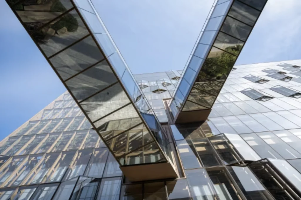 Looking upward at a modern glass office building with reflective surfaces and sky