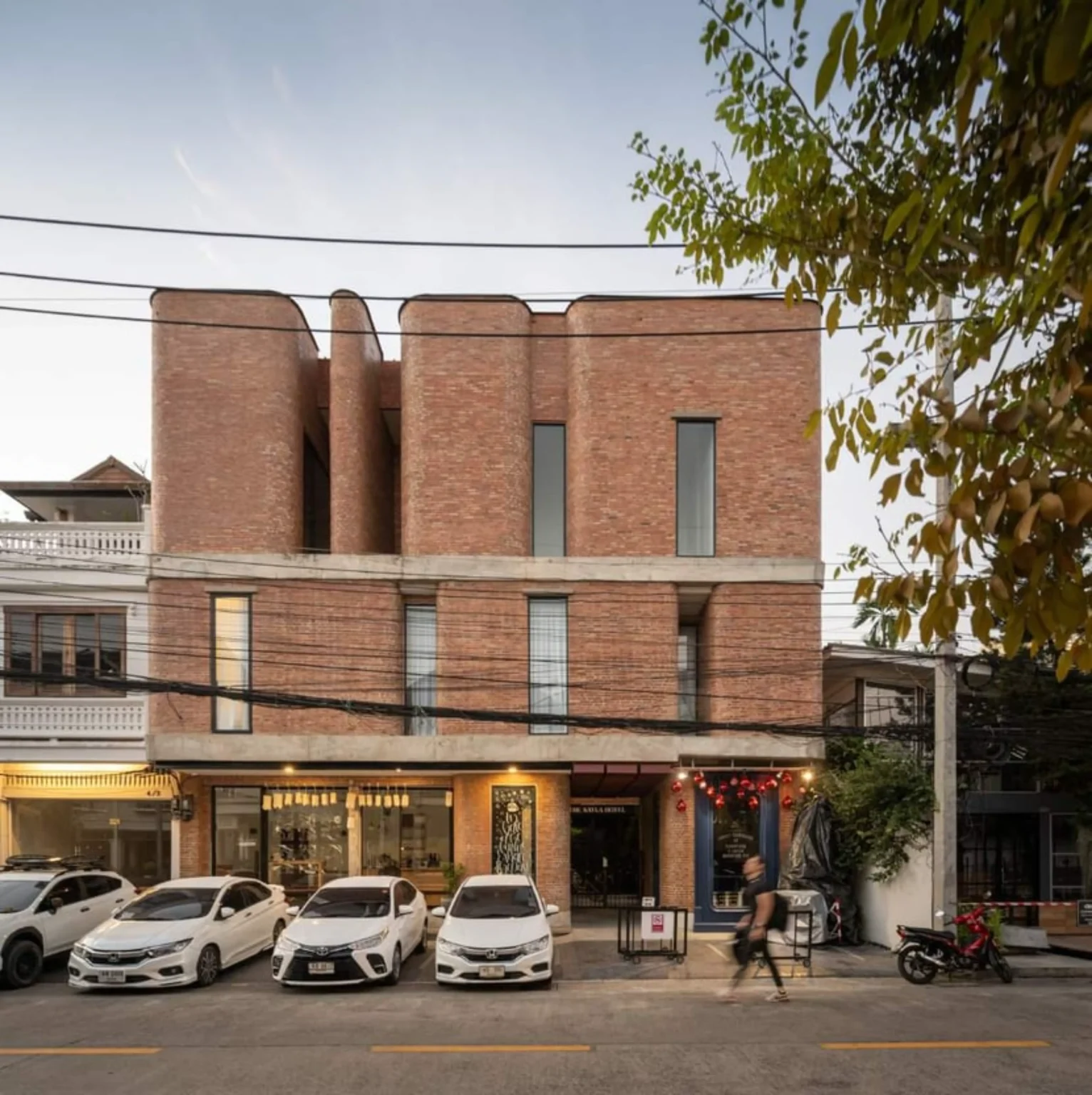 Street view of The Sayla Hotel showing the continuous red brick façade on a Chiang Mai soi