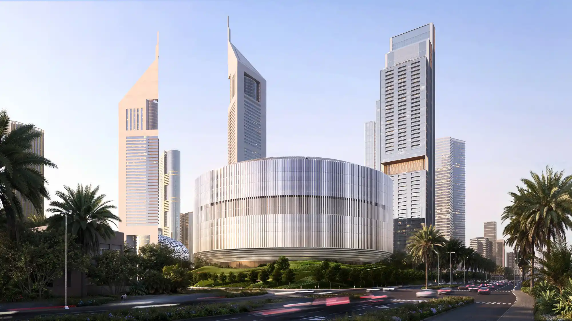 Ön planda palmiye ağaçları ve bulanık trafik akışı görülürken, Burj Khalifa ve diğer gökdelenlerin yer aldığı şehir manzarasında fütüristik dairesel bir bina hâkimiyet kuruyor.