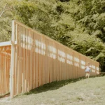 Side view of the pavilion showing the continuous wall of suspended timber battens set among trees