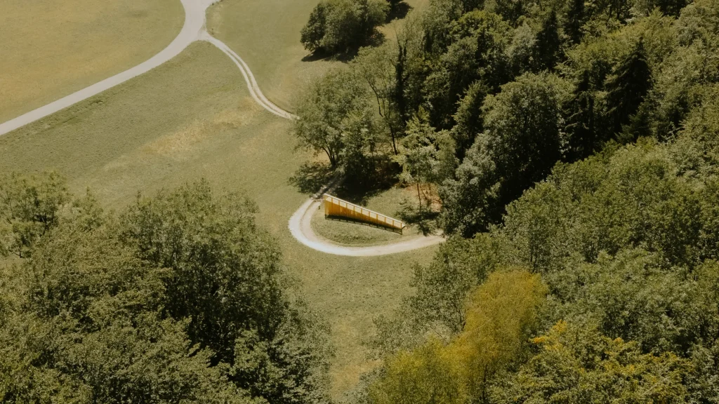 Aerial view of the pavilion as a thin linear mark across the green valley landscape