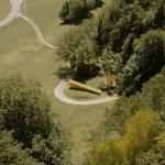 Aerial view of the pavilion as a thin linear mark across the green valley landscape