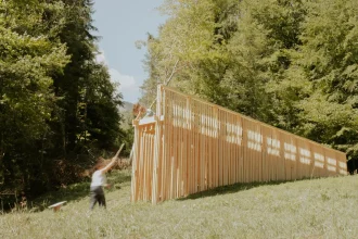 Distant view of the timber pavilion on the hillside with a person standing nearby