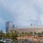 Night rendering of the diamond-patterned stadium beside a river, with a tall glass tower and crowds along the waterfront