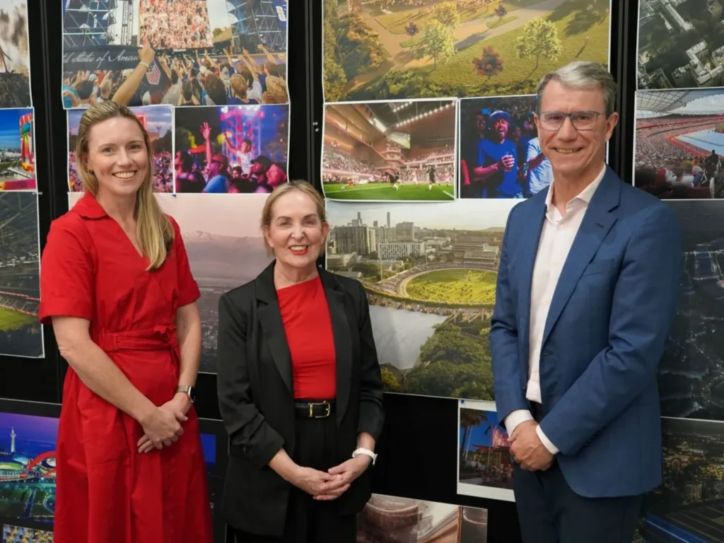 Three people standing in front of a wall of stadium project images and renderings