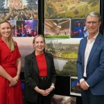 Three people standing in front of a wall of stadium project images and renderings