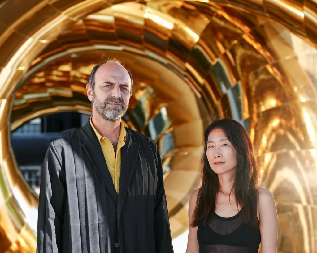 Artists Marco Canevacci and Yena Young standing inside the golden coils of auruBOROS