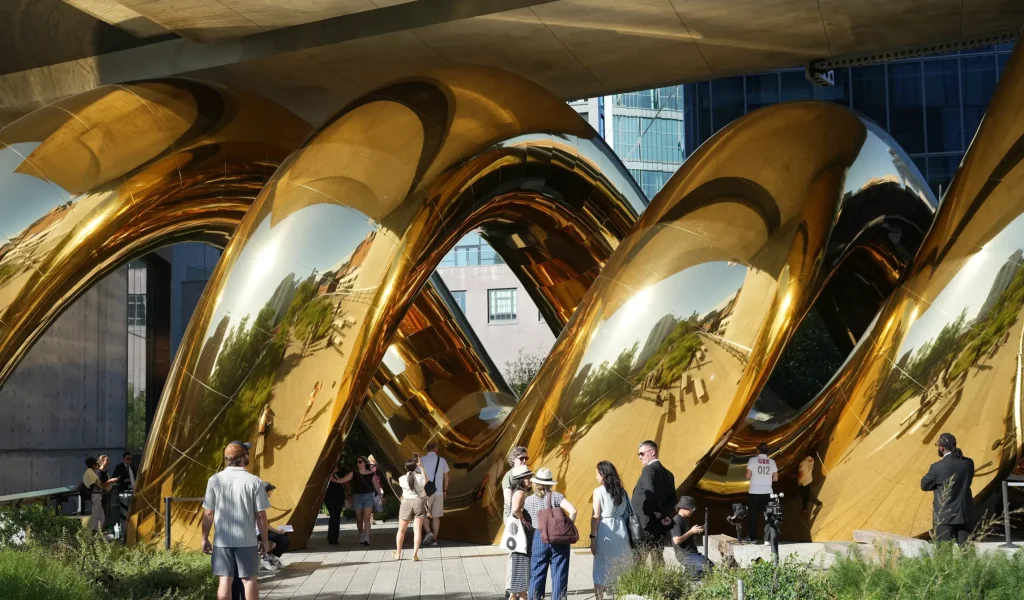 Wide view of the golden double-helix form of auruBOROS beneath the High Line and surrounding buildings