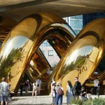 Wide view of the golden double-helix form of auruBOROS beneath the High Line and surrounding buildings