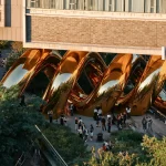 Side view of the interlocking golden volumes against brick buildings and trees