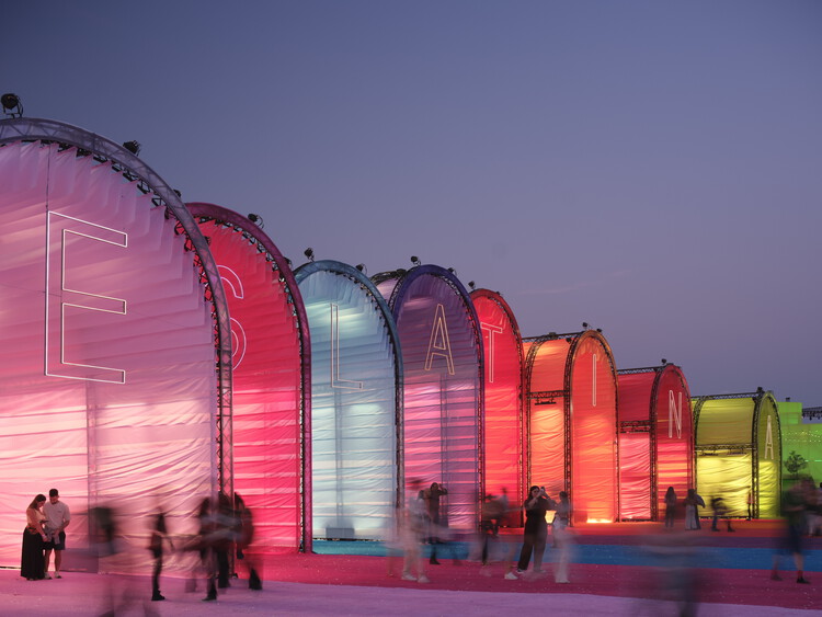 BIG Turns Madrid into Macondo Park for Shakira’s Residency_Row of illuminated arched fabric pavilions in pink, purple, blue, red, orange and yellow glowing at dusk