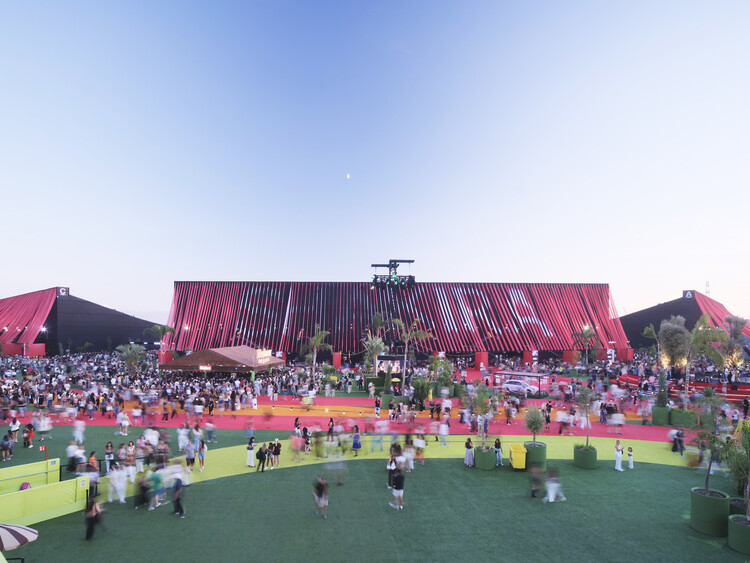 BIG Turns Madrid into Macondo Park for Shakira’s Residency_Large red fabric-clad stadium structure with crowds gathering on colorful ground surfaces at twilight