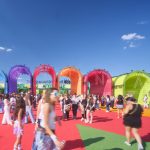 Daytime view of arched fabric pavilions spelling letters across a red plaza filled with visitors
