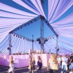 Interior of a pavilion with lavender fabric drapes suspended from a black truss structure