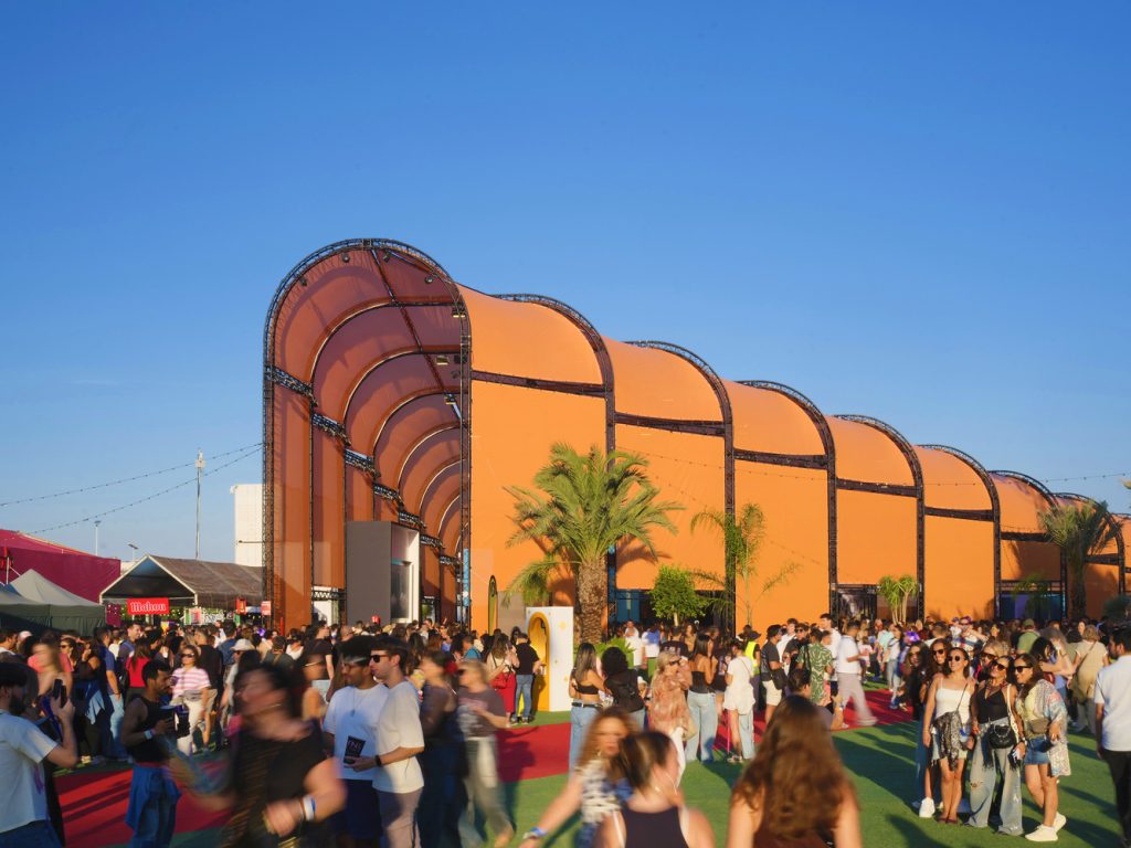BIG Turns Madrid into Macondo Park for Shakira’s Residency_Long orange arched pavilion under clear blue sky with crowds moving along the entrance area