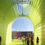 View through a bright yellow fabric tunnel framing the red stadium in the distance