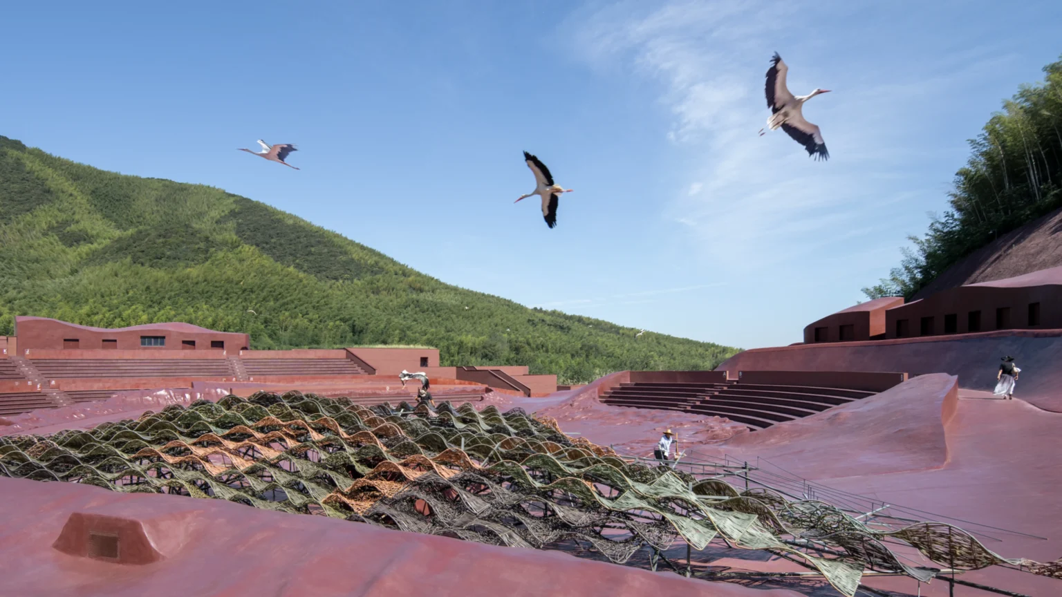 White storks flying above the open-air theater with woven stage structures in the foreground