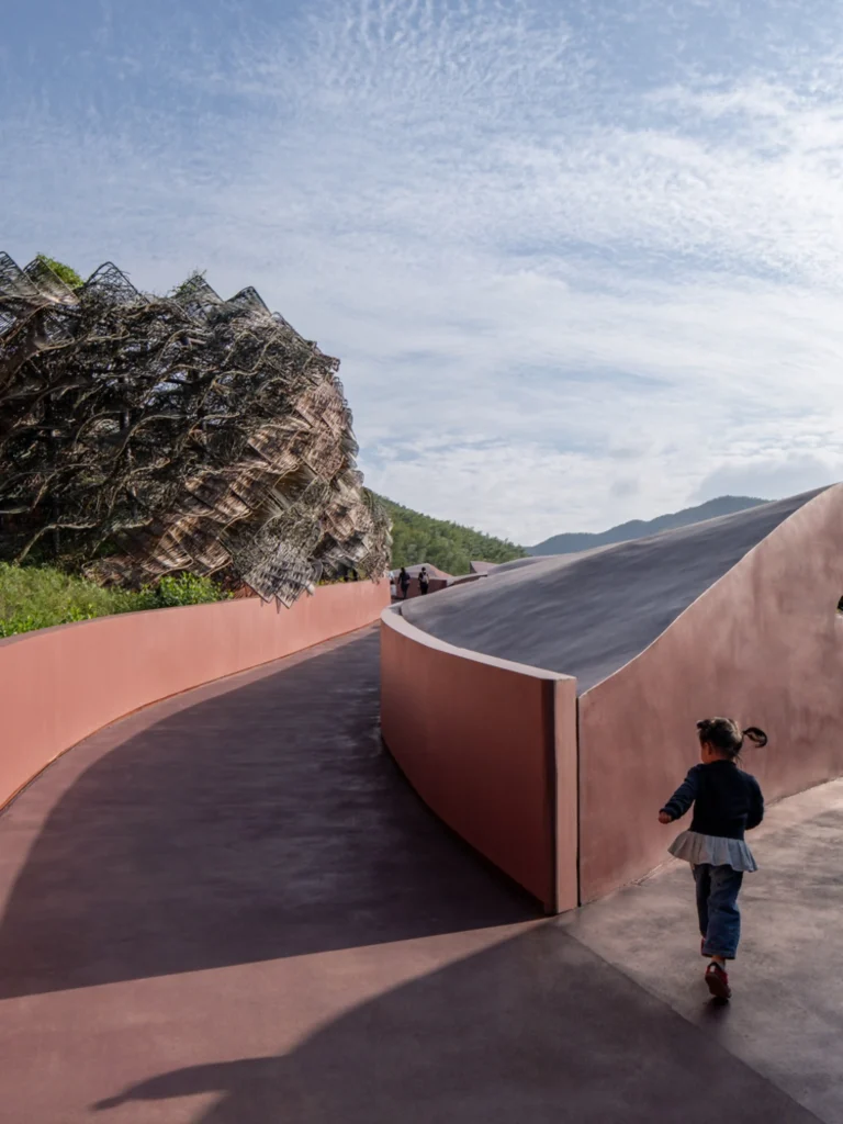 Earth Valley Theater: Young child running along a curved reddish path beside a large woven organic structure