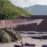 Person interacting with a stork near woven habitat structures and sculpted ground forms