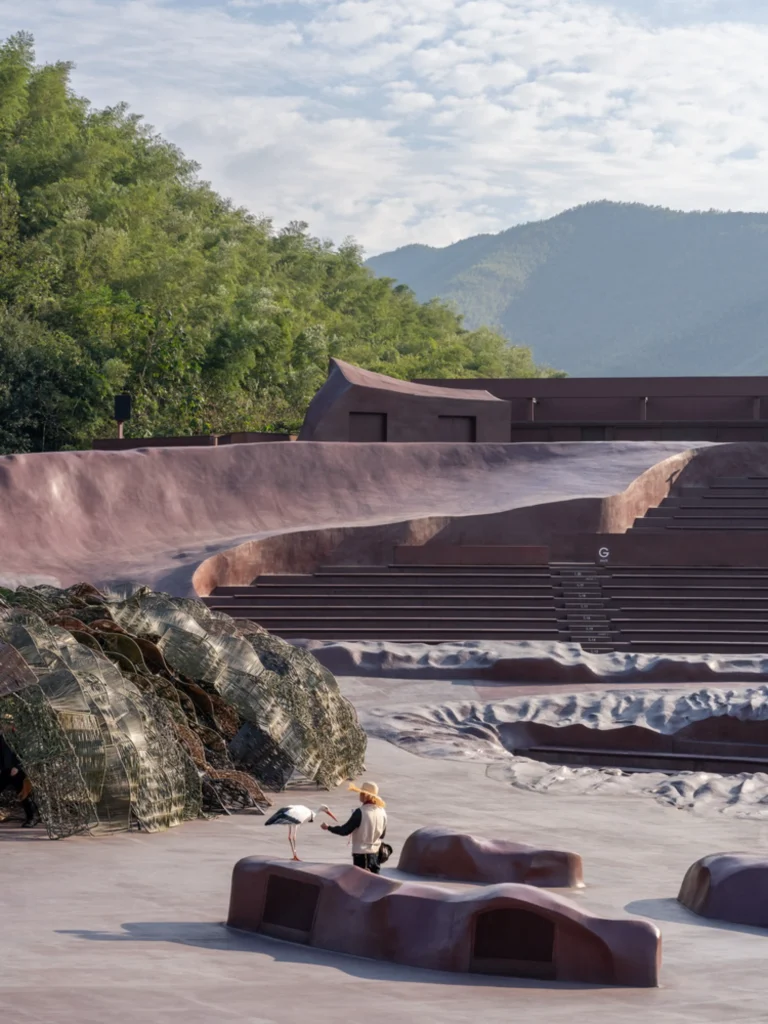 Earth Valley Theater: Person interacting with a stork near woven habitat structures and sculpted ground forms