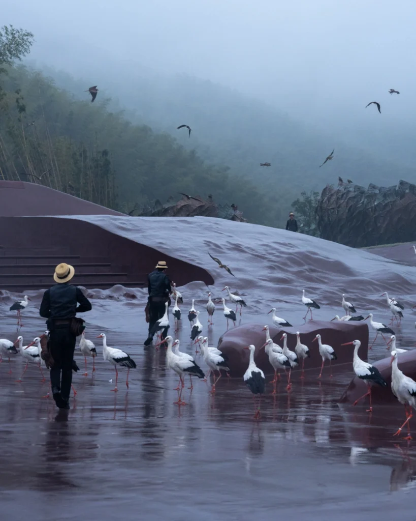 Earth Valley Theater: Handlers and a large flock of storks moving across the wet amphitheater floor in misty conditions