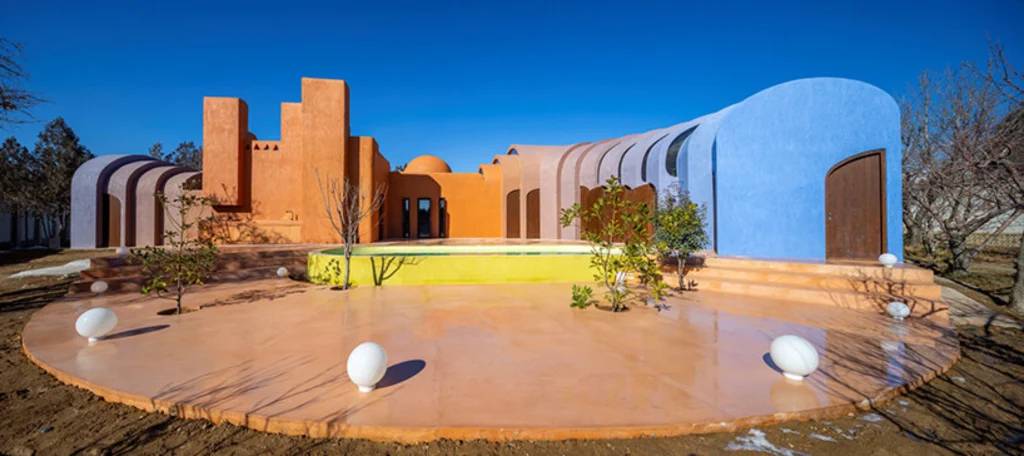 Exterior view of Gelareh House showing the original terracotta volume connected to blue vaulted extensions beside a pool