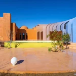Exterior view of Gelareh House showing the original terracotta volume connected to blue vaulted extensions beside a pool