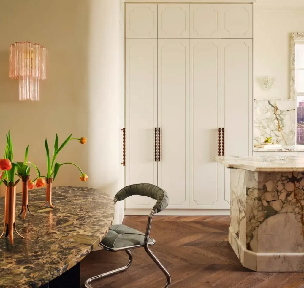 Elegant interior featuring custom cabinet handles on cream-colored cabinetry, a marble dining table, sculptural furniture, and natural wood flooring