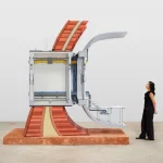 Large sectional model of a Mars habitat wall with exposed interior systems and a woman standing beside it for scale in a white gallery space
